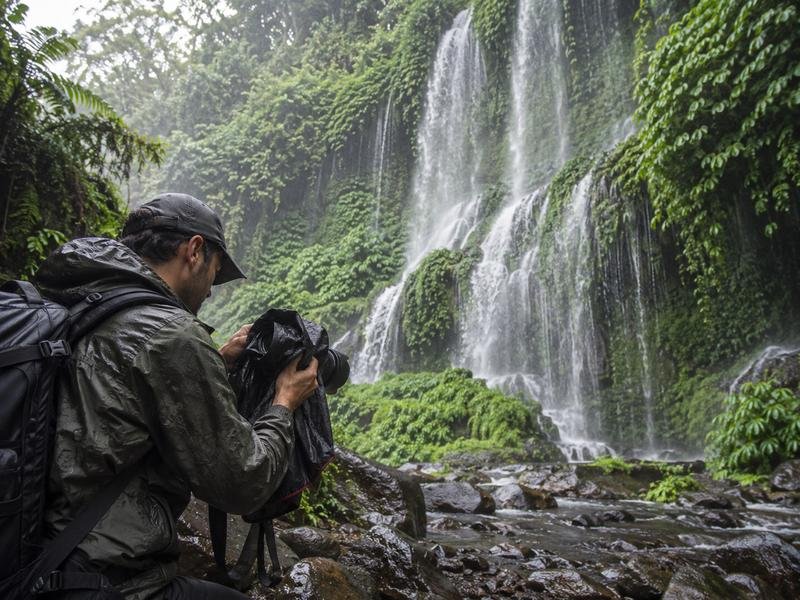 Photographer protecting camera gear from spray at Benang Kelambu